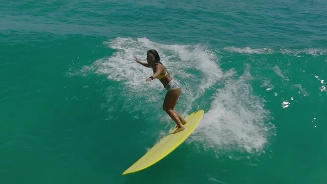 Asian woman surfing tropical ocean waves on longboard aerial drone shot