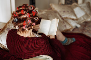 Fototapeta na wymiar Old active senior woman with rollers in hair take care of herself on her day off. Relaxing and resting on coach at home