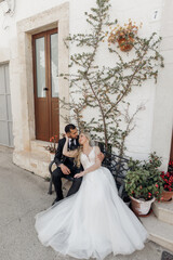 Vertical of wedding, married couple in love, sitting on the bench near doors of the church, hugging, waiting their turn