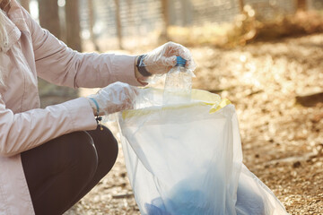 Cropped woman volunteer helping to clean nature from plastic waste. Collecting bottles to bag....