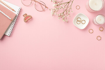 Business concept. Top view photo of workstation candles copybooks pencils stylish glasses gold rings hairpin and white gypsophila flowers on isolated pastel pink background with copyspace