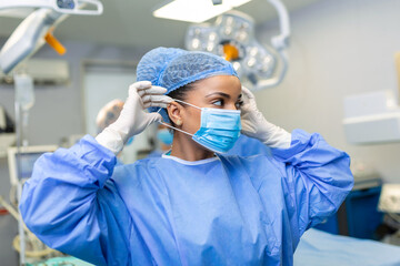Portrait of beautiful female doctor surgeon putting on medical mask standing in operation room....