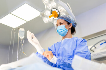 Portrait of beautiful female doctor surgeon putting on medical gloves standing in operation room....