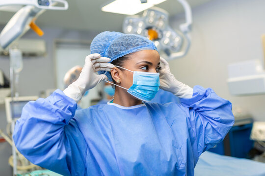 Portrait of beautiful female doctor surgeon putting on medical mask standing in operation room. Surgeon at modern operating room