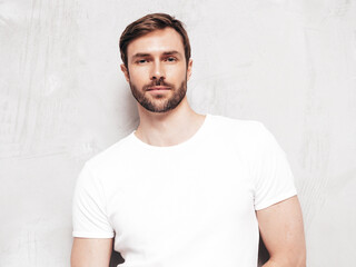 Obraz premium Portrait of handsome smiling stylish hipster lambersexual model. Sexy man dressed inT-shirt and jeans. Fashion male isolated on grey wall in studio
