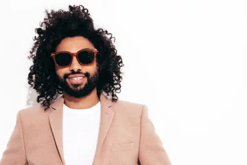 Handsome smiling hipster  model.Unshaven Arabian man dressed in elegant beige suit . Fashion male with long curly hairstyle posing near white wall in studio. Isolated. In sunglasses © halayalex