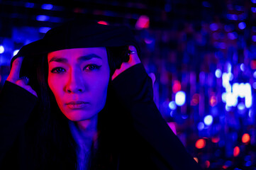 Close-up portrait of an androgenic model in a hood. Male transgender in studio with neon light.