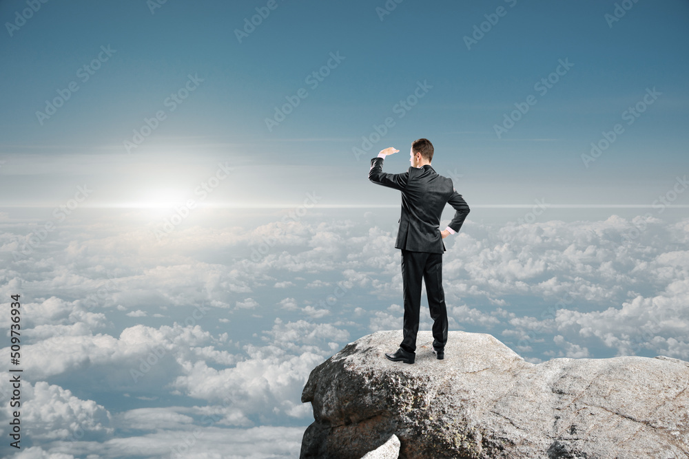 Poster businessman standing on cliff and looking into the distance on bright blue sky and clouds background