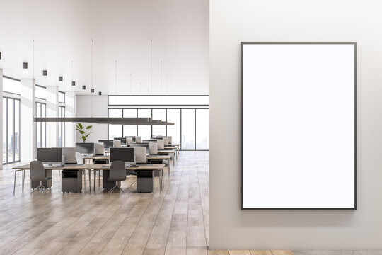 Blank white poster on light wall with place for your logo in spacious sunlit office area with cozy workspaces, high ceiling, panoramic windows with city view and wooden floor. 3D rendering, mockup