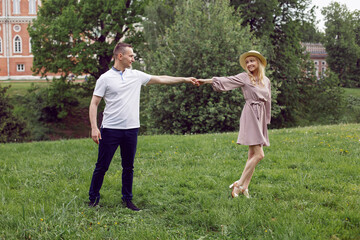 man and a woman in love in a dress and hat are walk on a green field under a tree in summer.