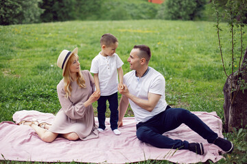 family with a child a boy of 4 years old sitting on a green field under a tree in summer on a blanket.