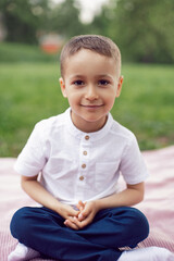 portrait of a four year old boy in a white shirt on a field in summer sit on cover.