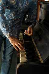 A glass of wine at a man's hand in front of a vintage piano