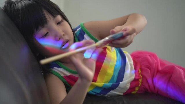Little Chinese girl try to open the plastic of lollipop sweet.