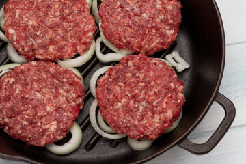 Raw beef burgers with chopped onions in frying pan