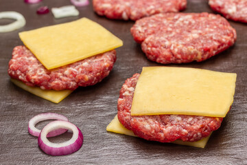 Raw beef burgers with cheese on brown background.