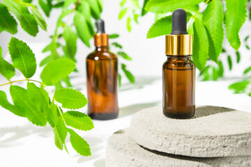 Serum, essential oil, tonic in a brown bottle on a white background with green leaves of the plant. Natural cosmetics, beauty care, skin treatment eco products.