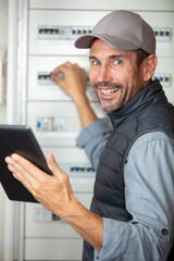 male electrician holding tablet and working on fuse box