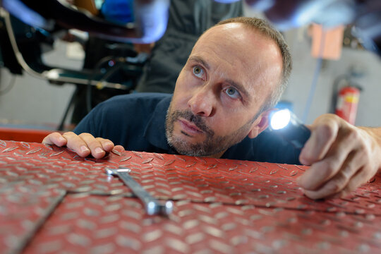 mechanic inspecting vehicle raised on chequerplate ramps
