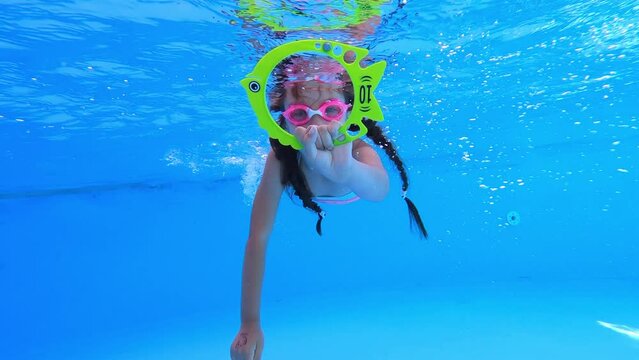 Little girl deftly swim underwater in pool. Child holds toy and moves forward. Sport good for healthy. Having fun in pool. Vacation and hobby.