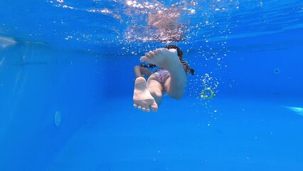 Little girl in blue bikini deftly swim underwater in pool by back side. Kid fast move legs and mades many air bubbles. Sport good for healthy. Vacation and hobby concept.