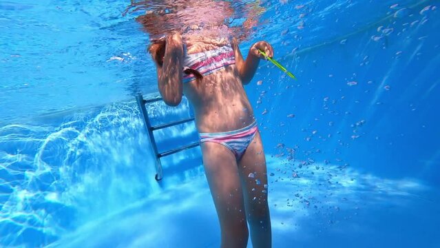 Little girl deftly swim with toy underwater in pool. Child in blue bikini  holds breath. Sport good for healthy. Having fun in the pool. Sunny summer day. Vacation and hobby concept.