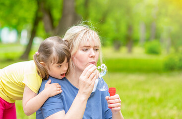 Woman and little girl with Downs syndrome  blow bubbles at summer park