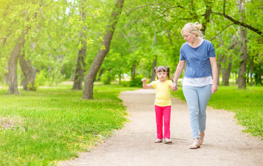 Fototapeta premium Little girl with syndrome down walks with her mother at sunny summer park. Empty space for text