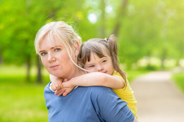 Young girl with special needs hugs her mother at sunny summer park