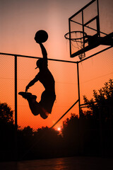 Basketball Player scoring an amazing slam dunk outdoors. Beautiful sunset view. Sun lights.  © Roman