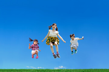 青空を背景にジャンプをする元気な幼い子供3人。健康,元気,仲良しのイメージ