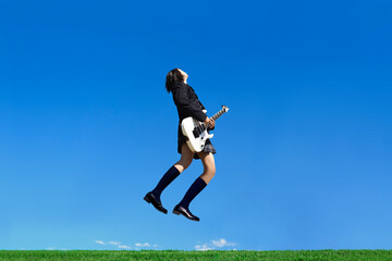 青空を背景にジャンプしながらギターを弾く女子高生の横姿