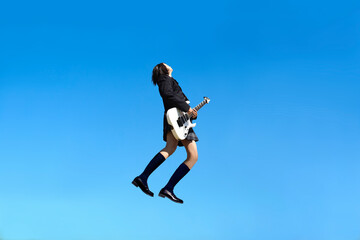 Fototapeta na wymiar 青空を背景にジャンプしながらギターを弾く女子高生の横姿