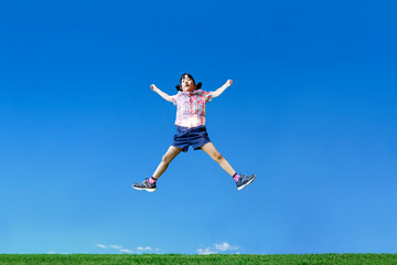 青空を背景に手足を広げジャンプする幼い女の子1人