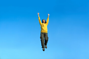 Fototapeta na wymiar 青空を背景に両手を上げてジャンプする中年女性