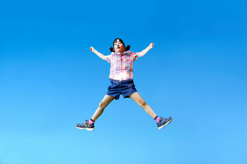 Obraz premium 青空を背景に手足を広げジャンプする幼い女の子1人
