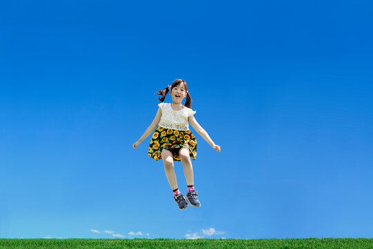 青空を背景に笑顔でジャンプする幼い女の子1人