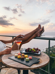 Beautiful female legs in heels overlooking the sea Aesthetic view. macarons. Coctail on the table