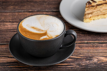 Relaxing latte coffee in black porcelain cup on wooden table