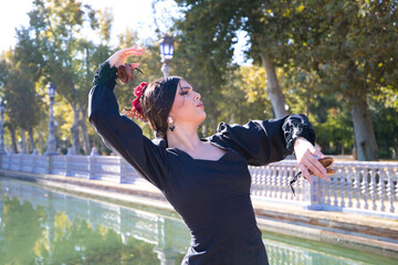 Woman dancing flamenco with black gypsy costume with yellow polka dots and red flower in her hair and castanets in her hands in seville. Concept of flamenco cultural heritage of humanity. - obrazy, fototapety, plakaty