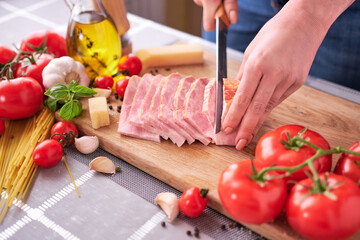 woman's hands slicing pancetta ham bacon on wooden cutting board at domestic kitchen