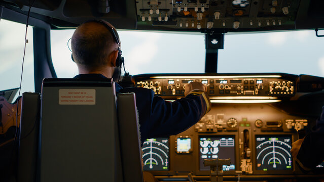 Male airline captain fixing altitude and longitude buttons, using dashboard navigation command and control panel. Flying airplane with aircrew and radar compass, power engine and windscreen.