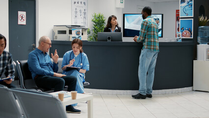 Reception desk with diverse patients waiting in lobby for checkup visit, people writing report at...