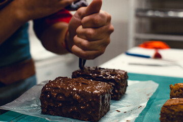 Close up of a hand putting some chocolate cream over a chocolate cake with pipping bag.