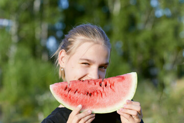 happy smiling teenage girl eating ripe juicy slice of watermelon in outdoor on green nature background