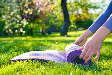 Young girl dressed in yoga clothes holding her eco-friendly yoga mat on the green grass in the park