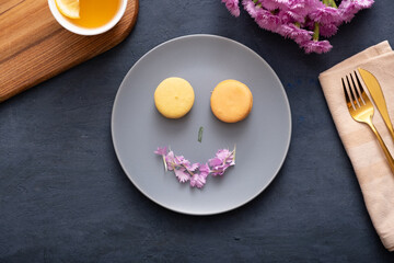 Smile with macaroons and petals on a plate on a dark stone table with flowers. Beautiful delicious dessert