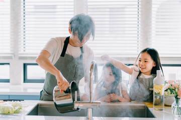台所で鍋を持つ父親と娘たち © Adobe Stock