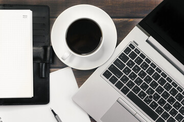 A cup of coffee with notebooks and a laptop computer on a wooden table.