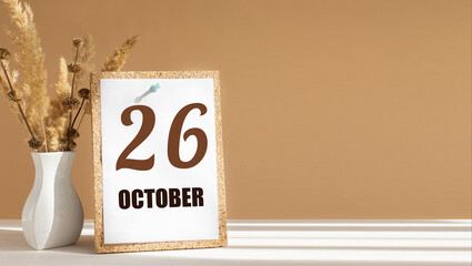 october 26. 26th day of month, calendar date.White vase with dead wood next to cork board with numbers. White-beige background with striped shadow. Concept of day of year, time planner, autumn month